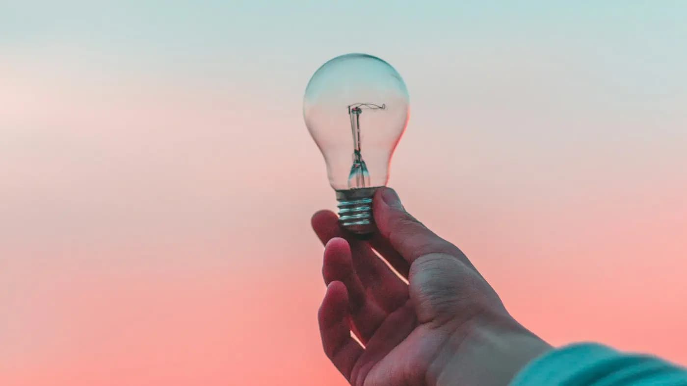 Hand holding a light bulb against a pastel sky
