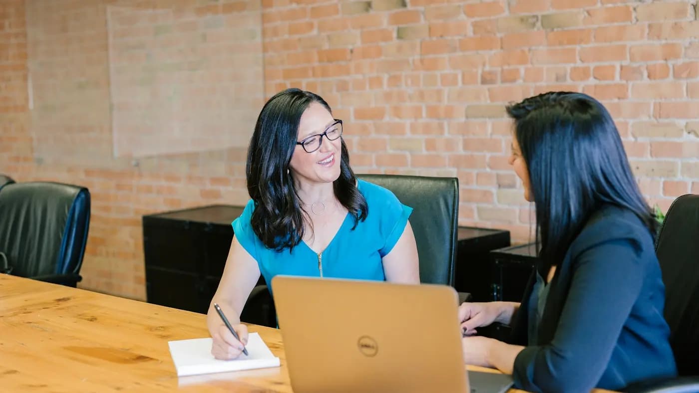 Two women discussing work at a table with a laptop