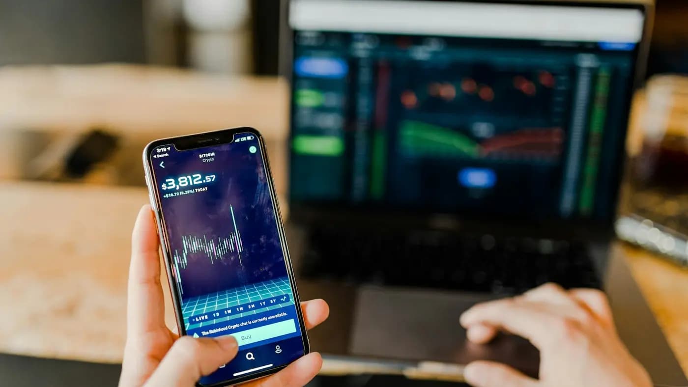 Phone showing a trading chart beside a laptop