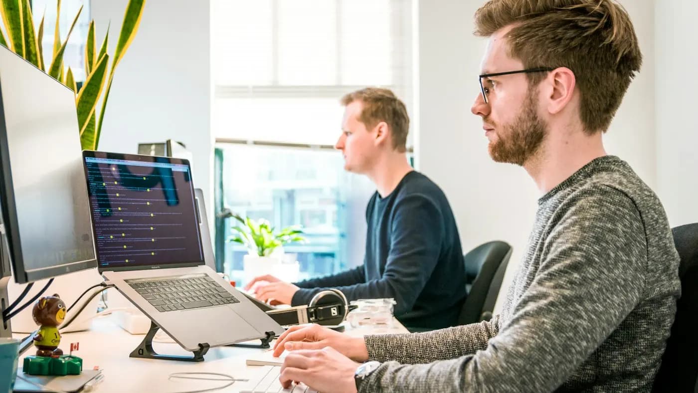 Two colleagues at laptops discussing work