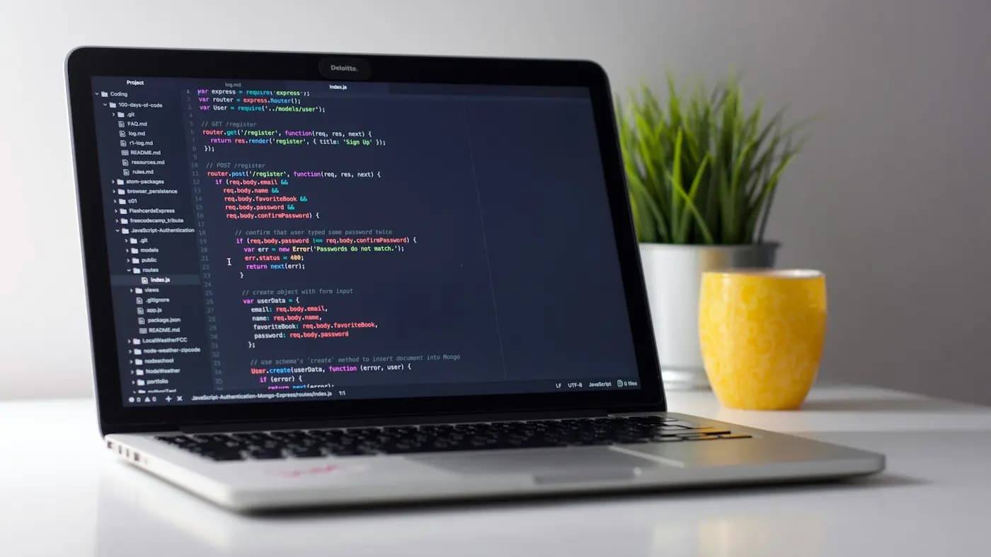 Laptop showing code beside a yellow mug and a plant