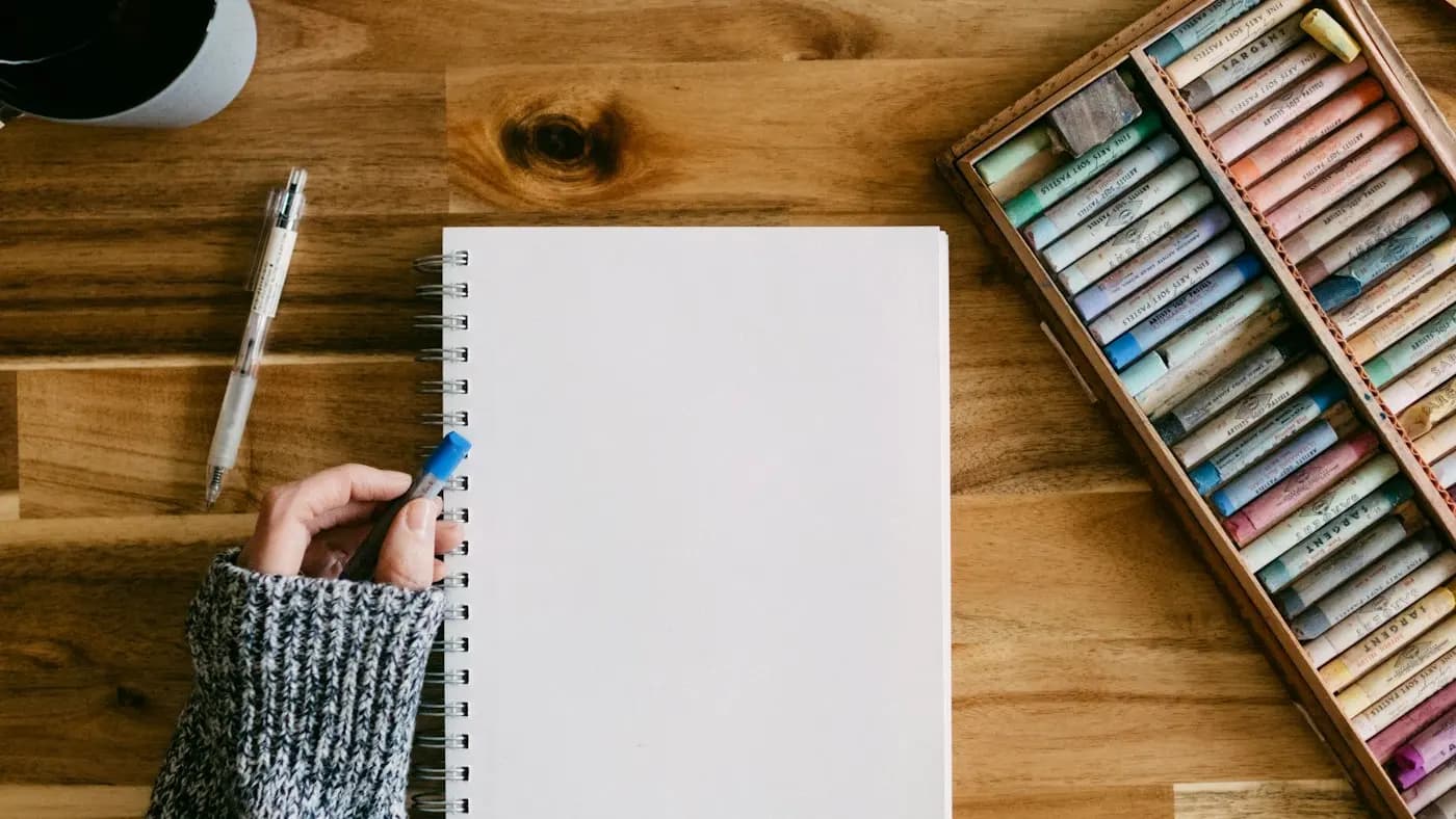 Blank notebook and pastels on a wooden desk