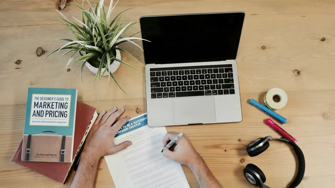 Hands writing notes next to a marketing book on a desk