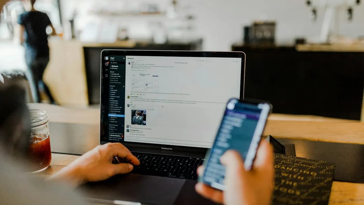 Person holding a smartphone while working on a laptop